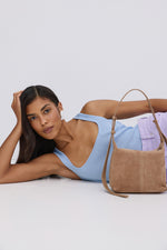 Model posiert in einem hellblauen Oberteil und trägt die beigefarbene Veloursleder-Schultertasche