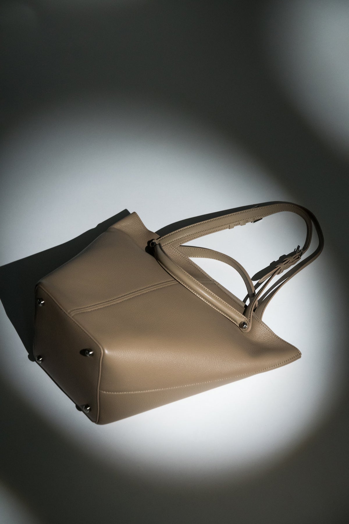 Künstlerische Produktaufnahme der beigen Ledertasche mit dynamischen Schattenwürfen 