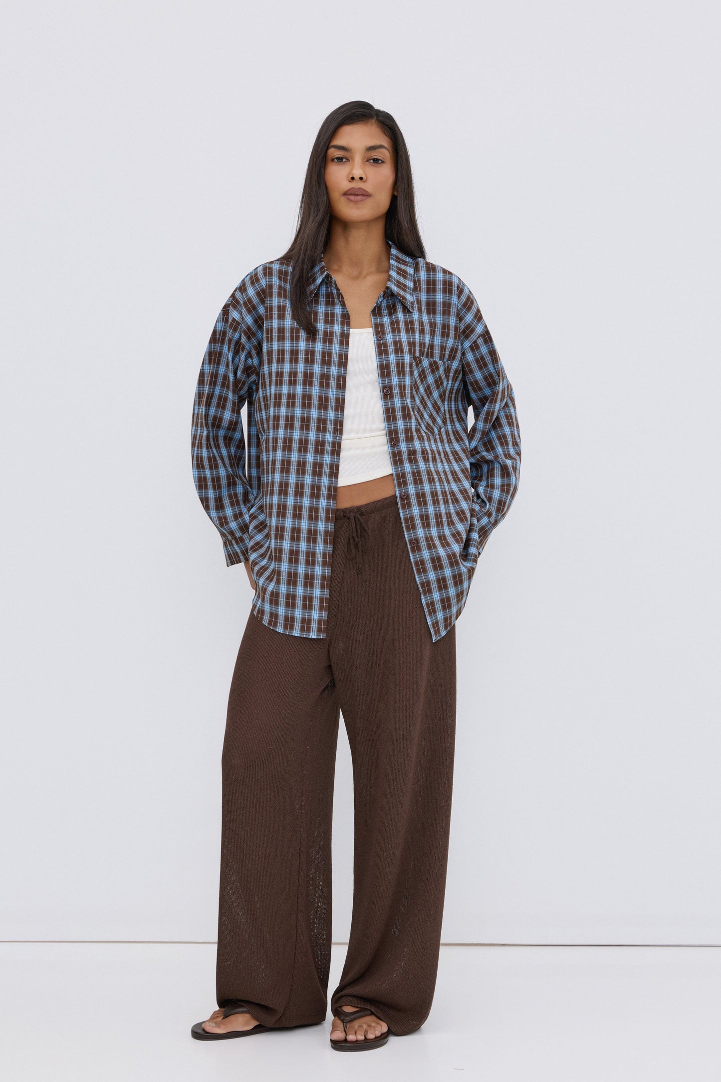 Frontansicht des Models, das die blau-braune Karo-Bluse über einem weißen Top und braunen Hosen trägt