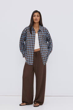 Frontansicht des Models, das die blau-braune Karo-Bluse über einem weißen Top und braunen Hosen trägt