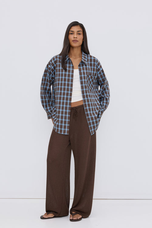 Frontansicht des Models, das die blau-braune Karo-Bluse über einem weißen Top und braunen Hosen trägt