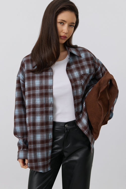 Modell präsentiert das Karohemd offen als Layering-Look über einem weißen Top