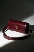 Künstlerische Aufnahme der bordeauxroten Leder-Clutch mit breitem Schulterriemen im Spotlight
