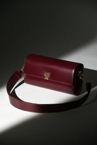 Künstlerische Aufnahme der bordeauxroten Leder-Clutch mit breitem Schulterriemen im Spotlight