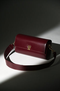 Künstlerische Aufnahme der bordeauxroten Leder-Clutch mit breitem Schulterriemen im Spotlight