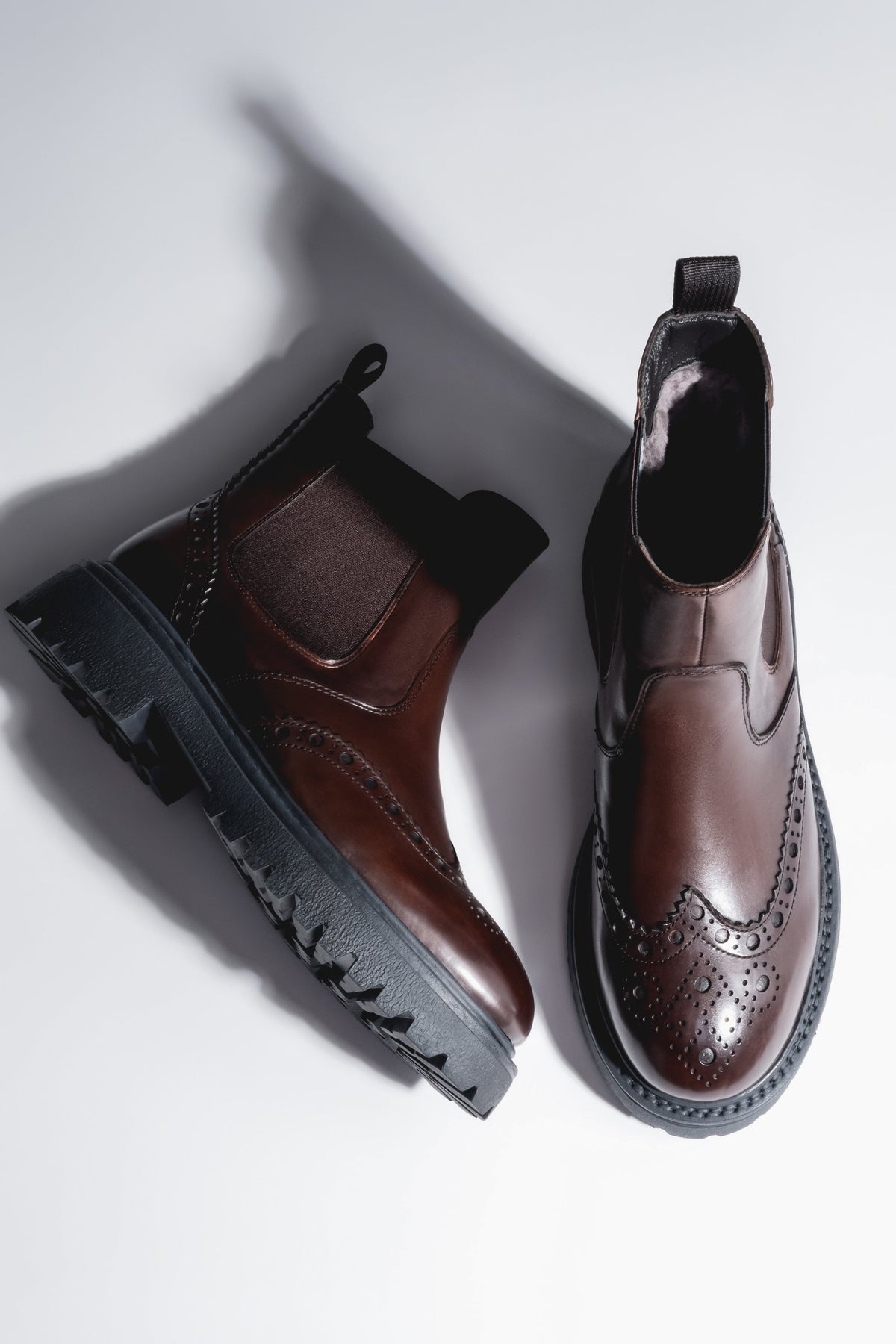 Künstlerische Draufsicht auf das Paar brauner Chelsea-Boots mit markanter Brogue-Lochung