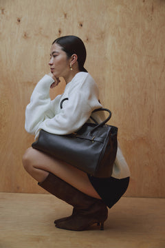 Model hockt und zeigt die flexiblen braunen Veloursstiefel in einem eleganten, urbanen Look