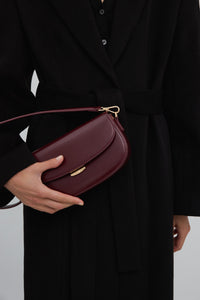 Das Model präsentiert die burgunderrote Estro Schultertasche aus Leder in Hufeisenform.