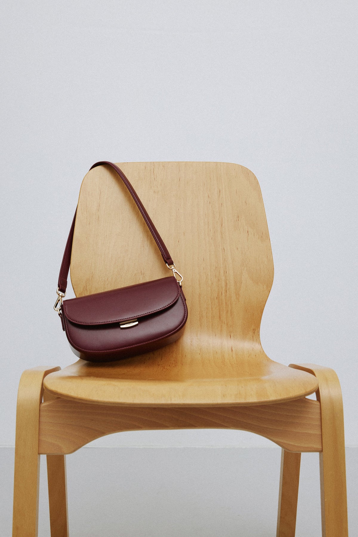 Die burgunderrote Ledertasche präsentiert auf einem Holzstuhl zur Darstellung der Größe.