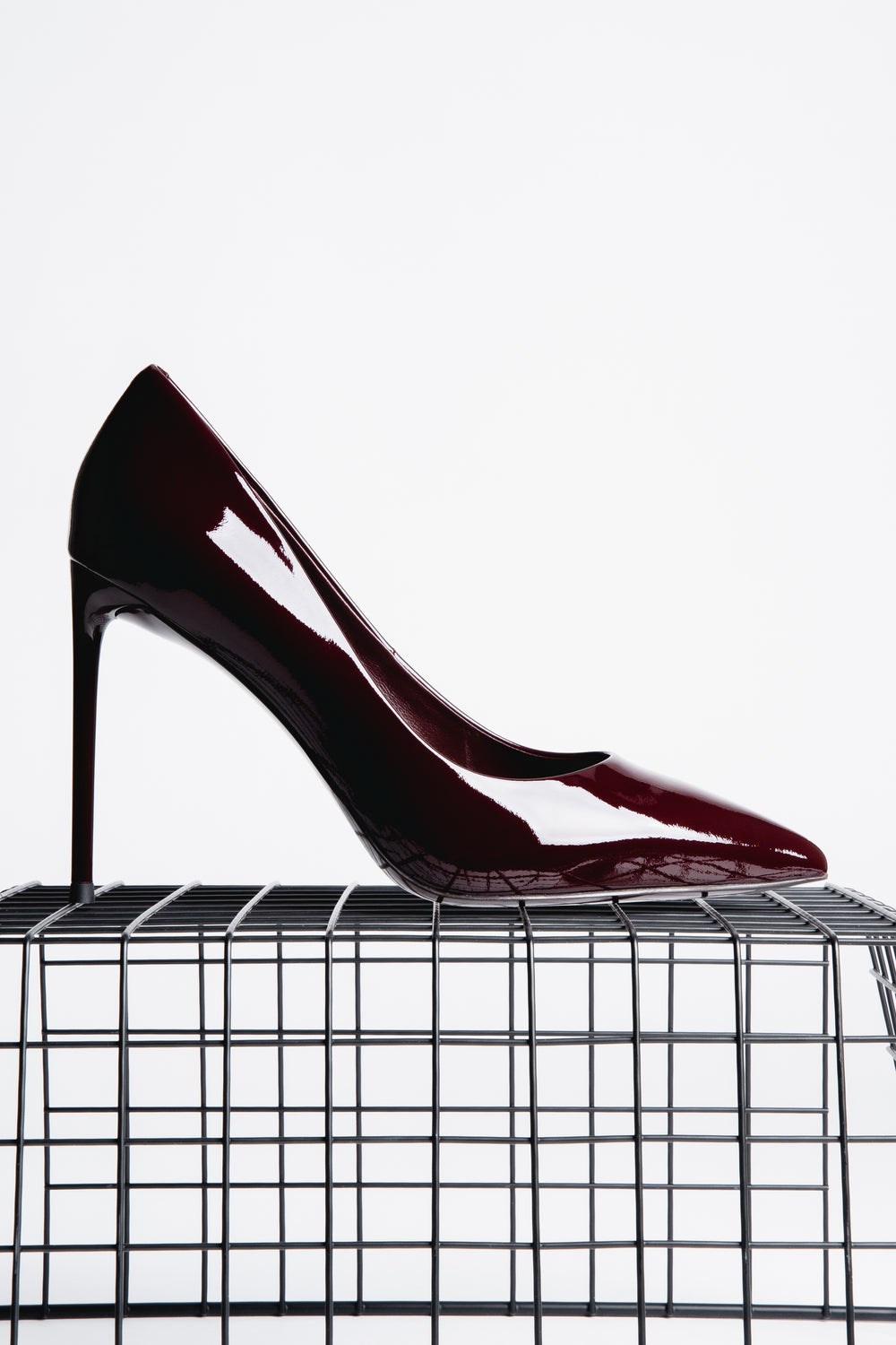 Profilansicht des burgundroten Lackleder-Stilettos auf einem schwarzen Gitterwürfel vor hellem Hintergrund