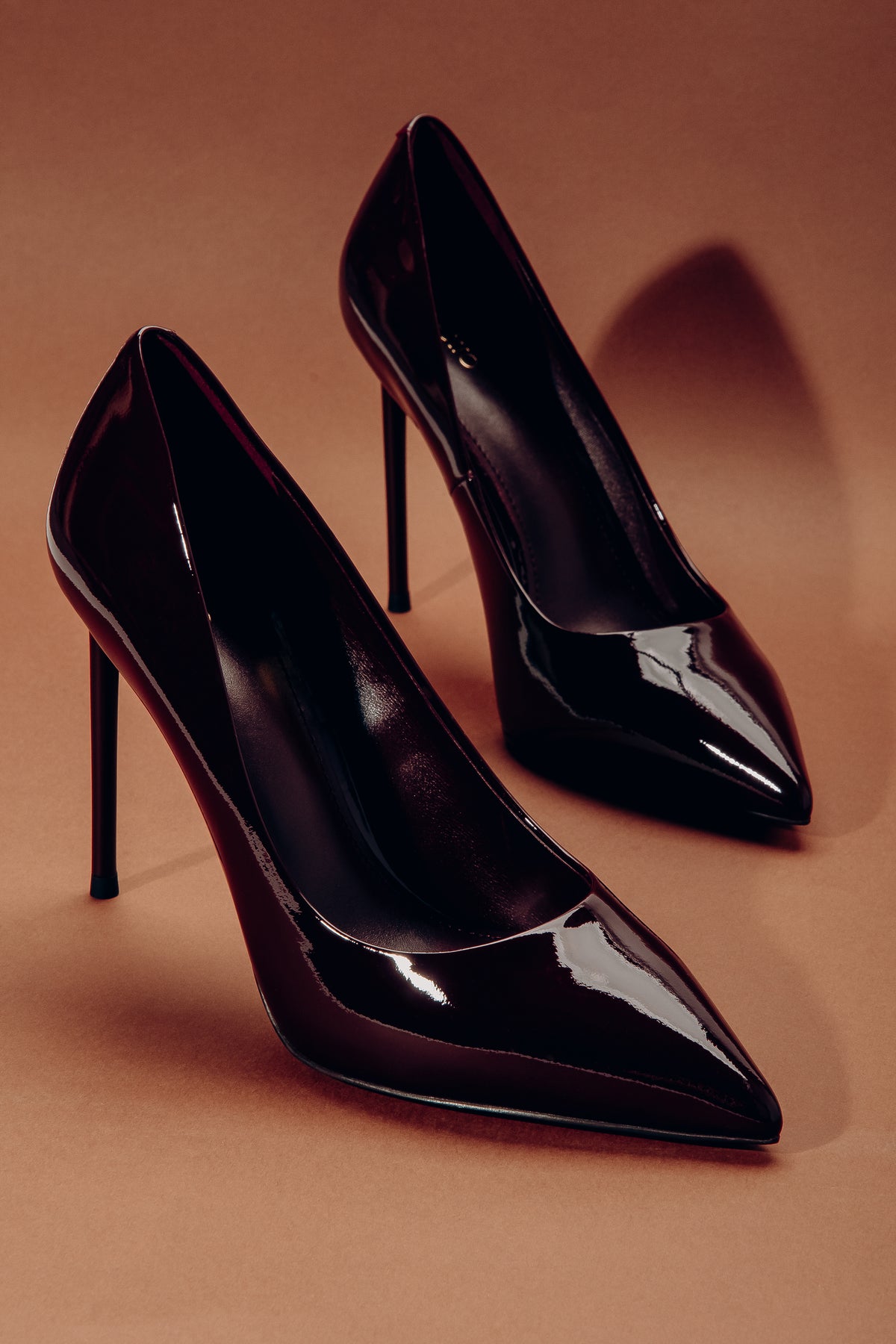 Elegantes Paar schwarzer Lackleder-Stilettos in harmonischer Anordnung vor warmem, sanftem Studiolicht