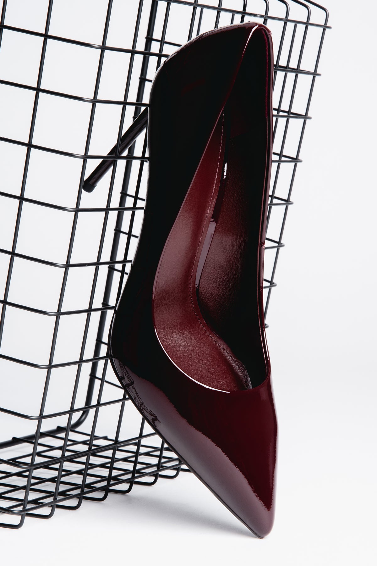 Schräge Ansicht des burgundroten Stilettos, der dekorativ an einem schwarzen Metallgitter lehnt