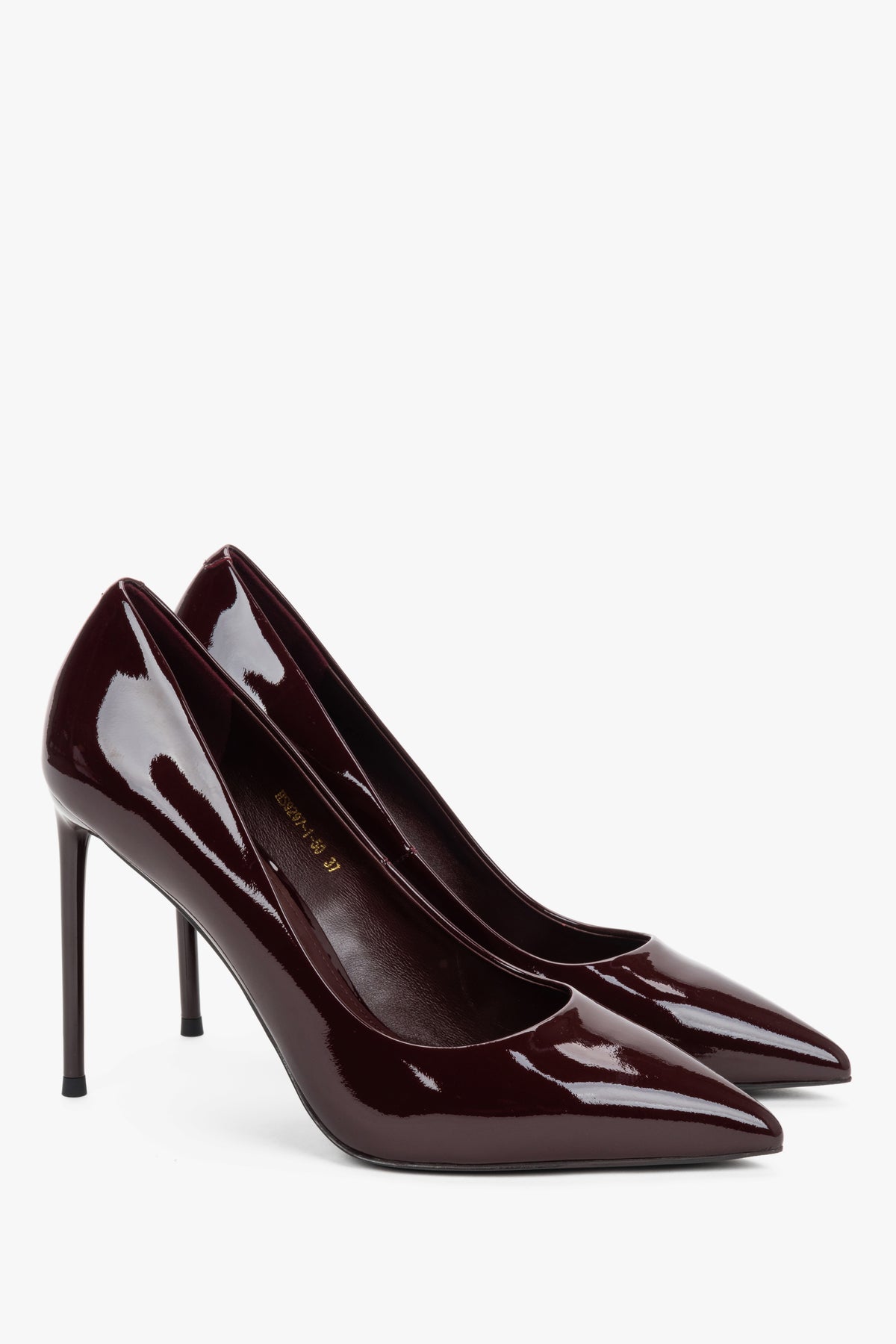 Zwei burgundrote Lackleder-Stilettos in eleganter, leichter Verschränkung auf hellem Grund