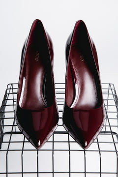 Frontalansicht von oben auf zwei burgundrote Stilettos auf einem schwarzen Gitterregal