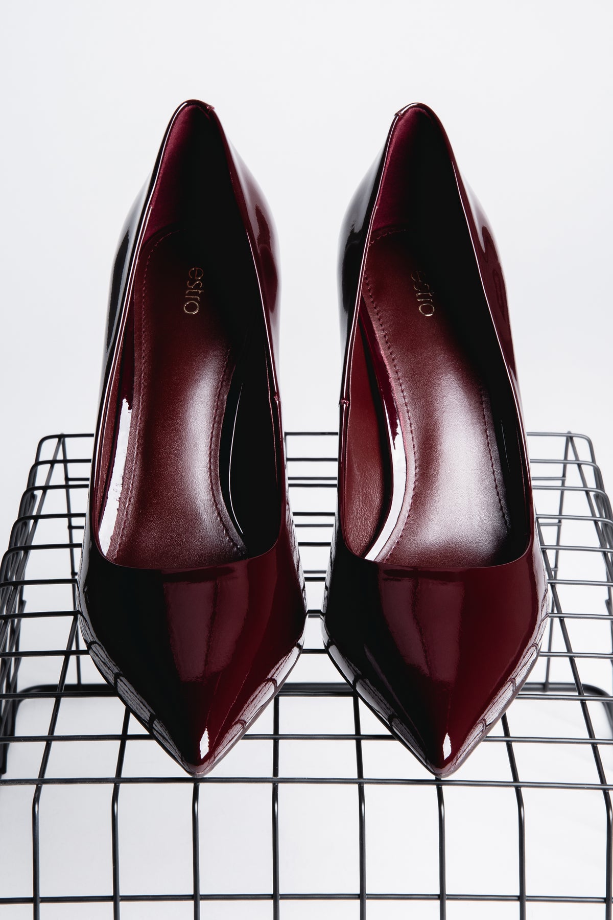 Frontalansicht von oben auf zwei burgundrote Stilettos auf einem schwarzen Gitterregal