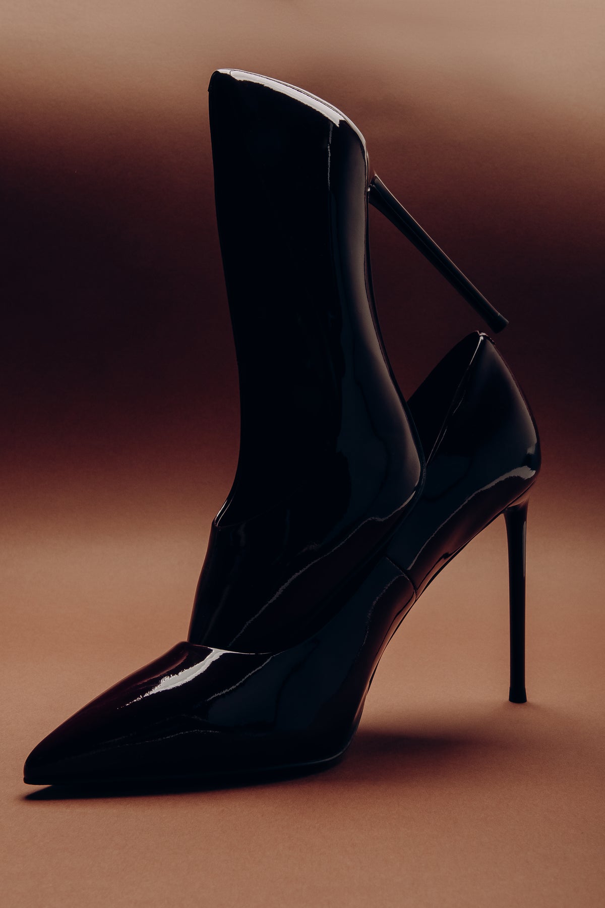 Kunstvolle, dramatische Perspektive eines schwarzen Lackleder-Stilettos mit hohem Absatz im Warmlicht-Studio