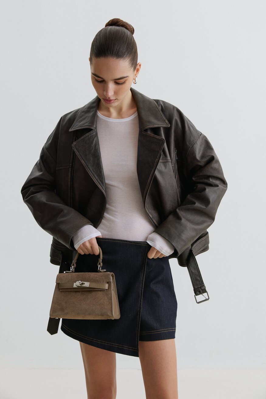 Model mit dunkler Jacke und Rock präsentiert die dunkelbeige Koffer-Handtasche aus italienischem Velours
