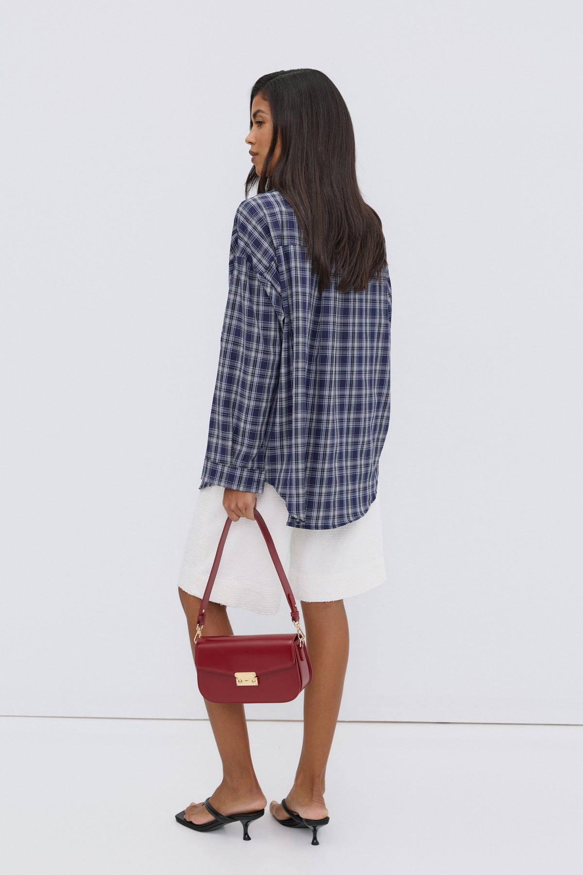 Rückansicht des Models in der überschnittenen, dunkelblau karierten Oversize-Bluse mit einer roten Handtasche