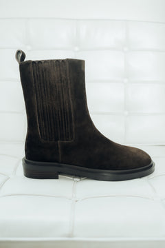 Dunkelbrauner Damen-Chelsea-Boot aus Veloursleder, seitlich präsentiert auf einem weißen Polstersessel