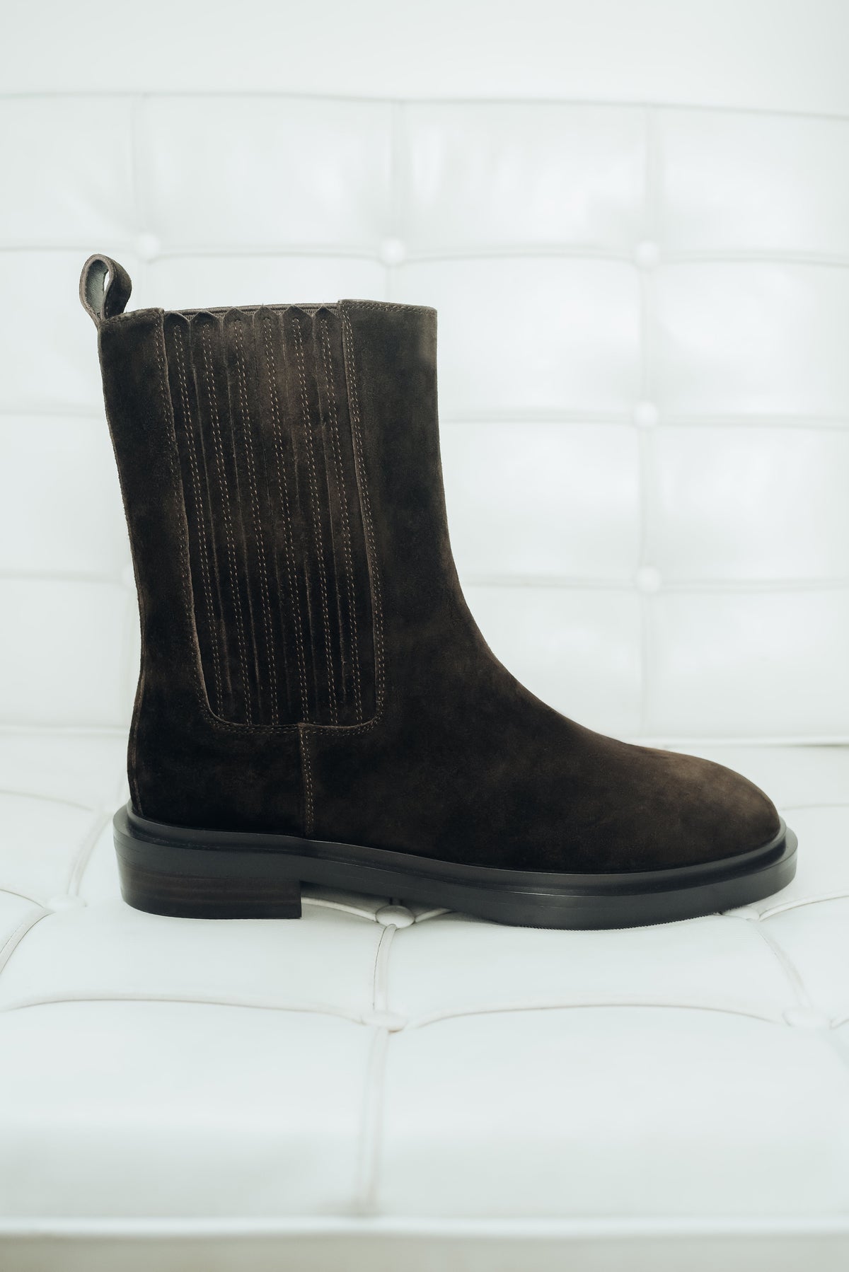 Dunkelbrauner Damen-Chelsea-Boot aus Veloursleder, seitlich präsentiert auf einem weißen Polstersessel
