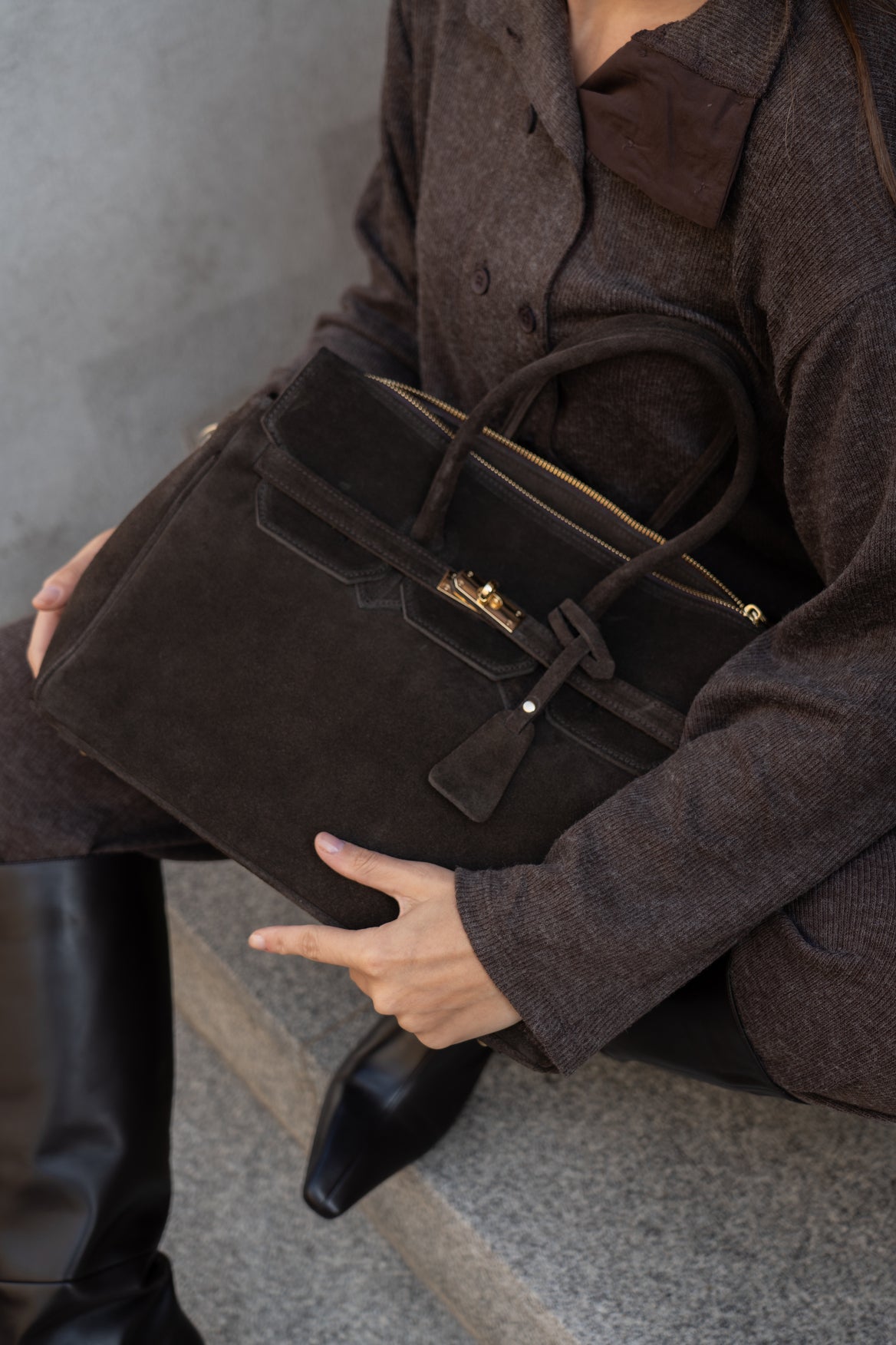 Lifestyle-Perspektive: Draufsicht auf das Model, das die dunkelbraune Velours-Henkeltasche elegant an den Griffen hält