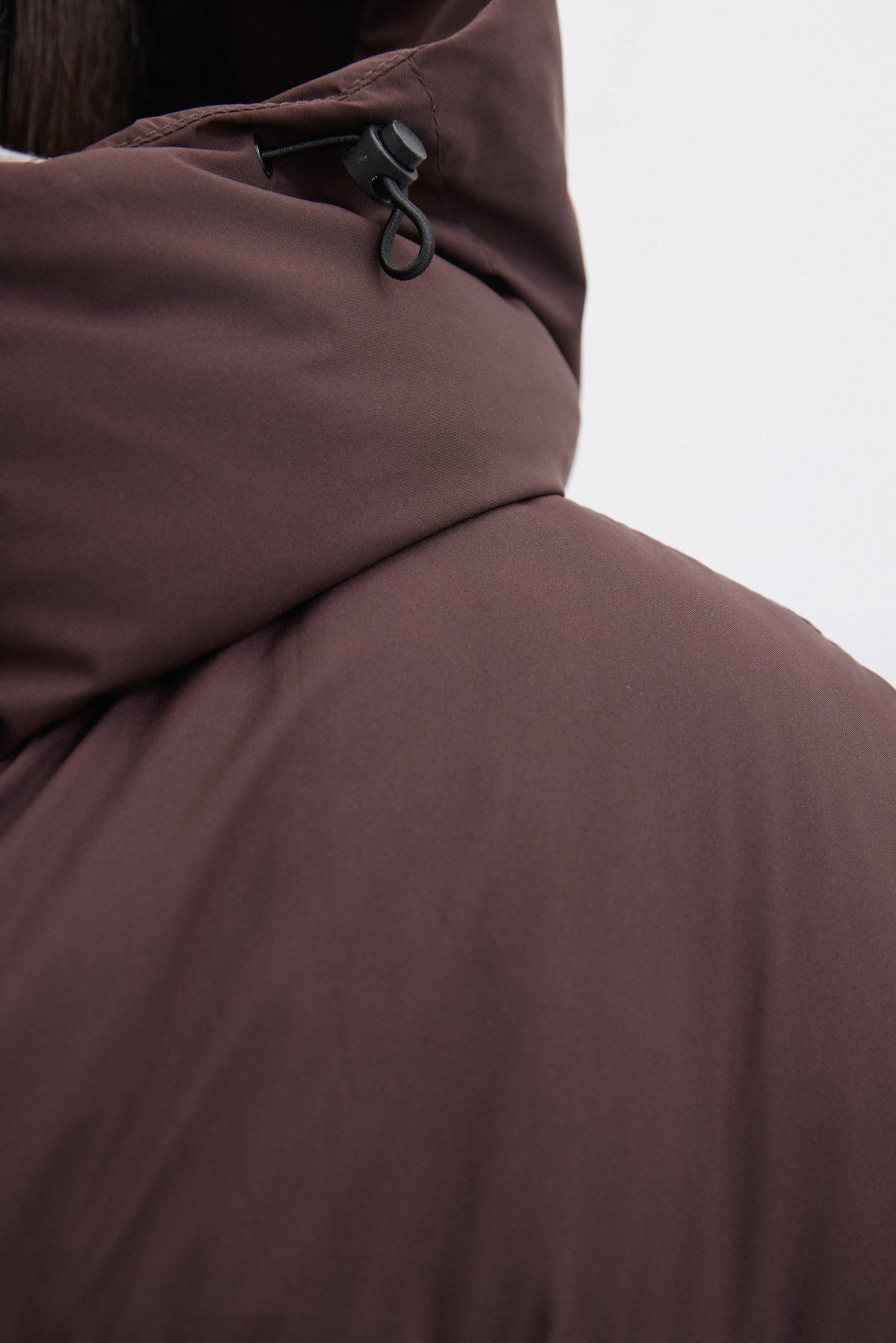 Detailaufnahme des hohen Stehkragens und der Kapuze der dunkelbraunen Pufferjacke 