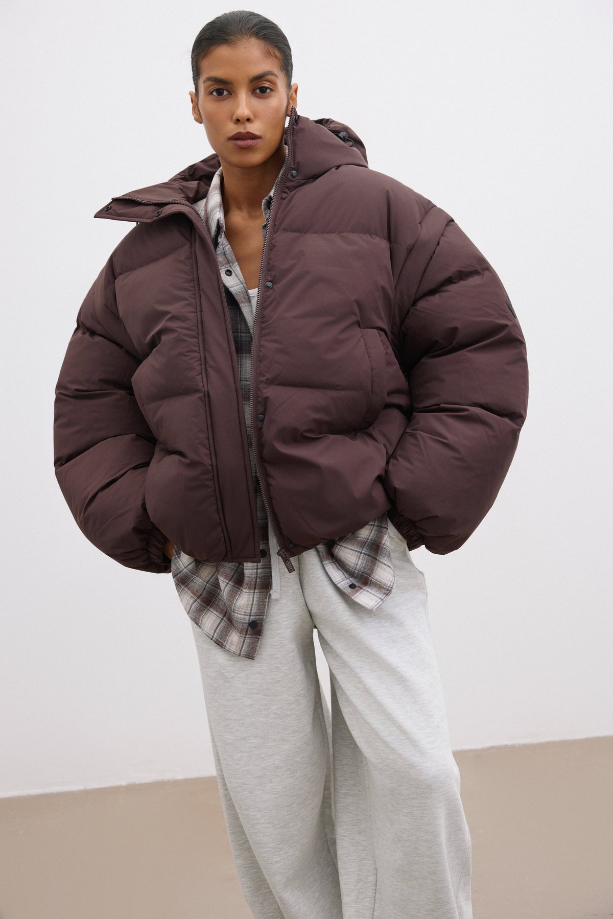 Leichte Schrägansicht der dunkelbraunen Jacke, die den Oversize-Schnitt und die große Kapuze zeigt 