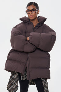 Model präsentiert die dunkelbraune Oversize-Pufferjacke mit Brille und Schal-Detail
