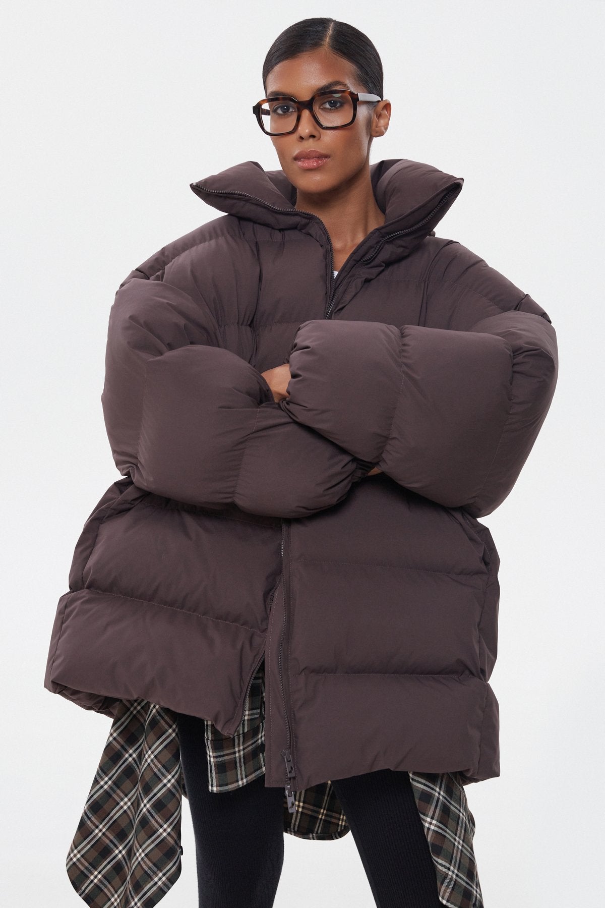 Model präsentiert die dunkelbraune Oversize-Pufferjacke mit Brille und Schal-Detail