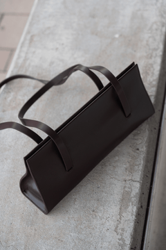 Draufsicht auf die flach auf einer Betonfläche im Freien liegende dunkelbraune Echtledertasche