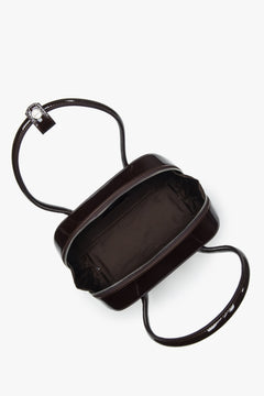 Draufsicht auf die geöffnete Lackledertasche mit Reißverschluss und Logo-Pin am Griff.