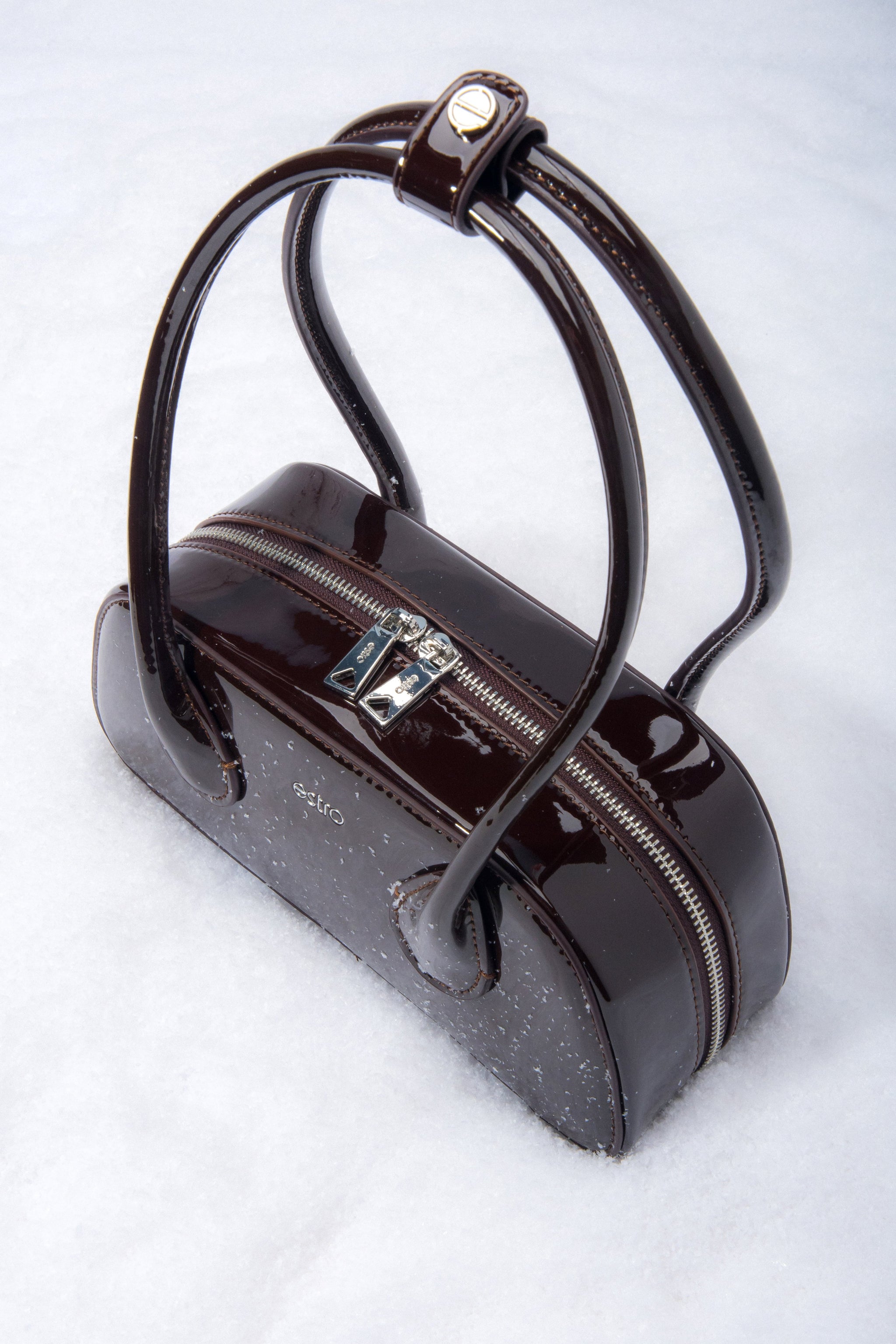 Detailaufnahme des Logo-Pins am Griff der dunkelbraunen Lackledertasche.