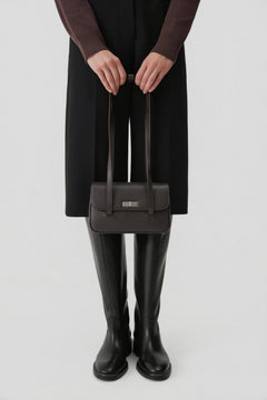 Model in dunklem Outfit hält die formstabile Ledertasche lässig in der Hand