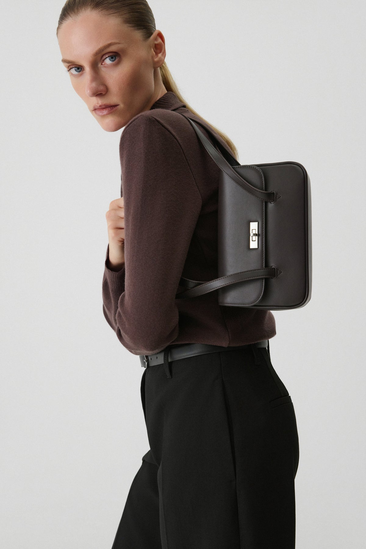 Model in schwarzer Hose hält die klassische Tasche eng unter dem Arm