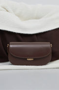 Dunkelbraune Damen-Schultertasche aus Leder in Hufeisenform auf weißem Strickstoff.