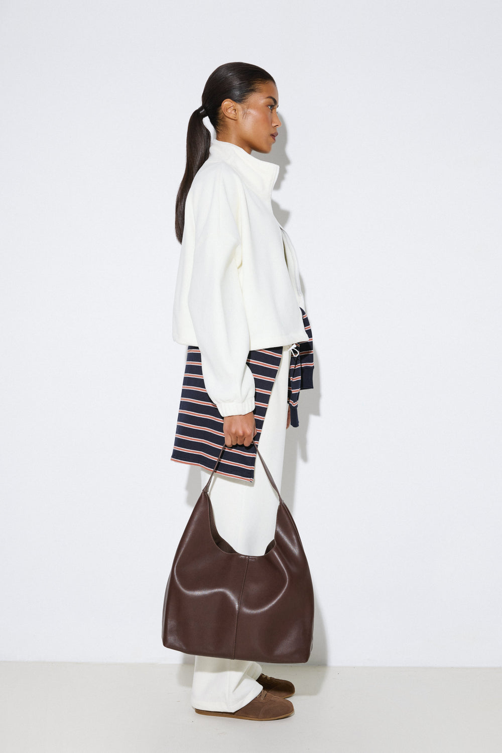 Stilvolle Profilaufnahme eines Models in heller Fleece-Jacke und weißen Hosen, das den dunkelbraunen Damen-Shopper aus echtem Leder präsentiert.