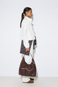 Stilvolle Profilaufnahme eines Models in heller Fleece-Jacke und weißen Hosen, das den dunkelbraunen Damen-Shopper aus echtem Leder präsentiert.