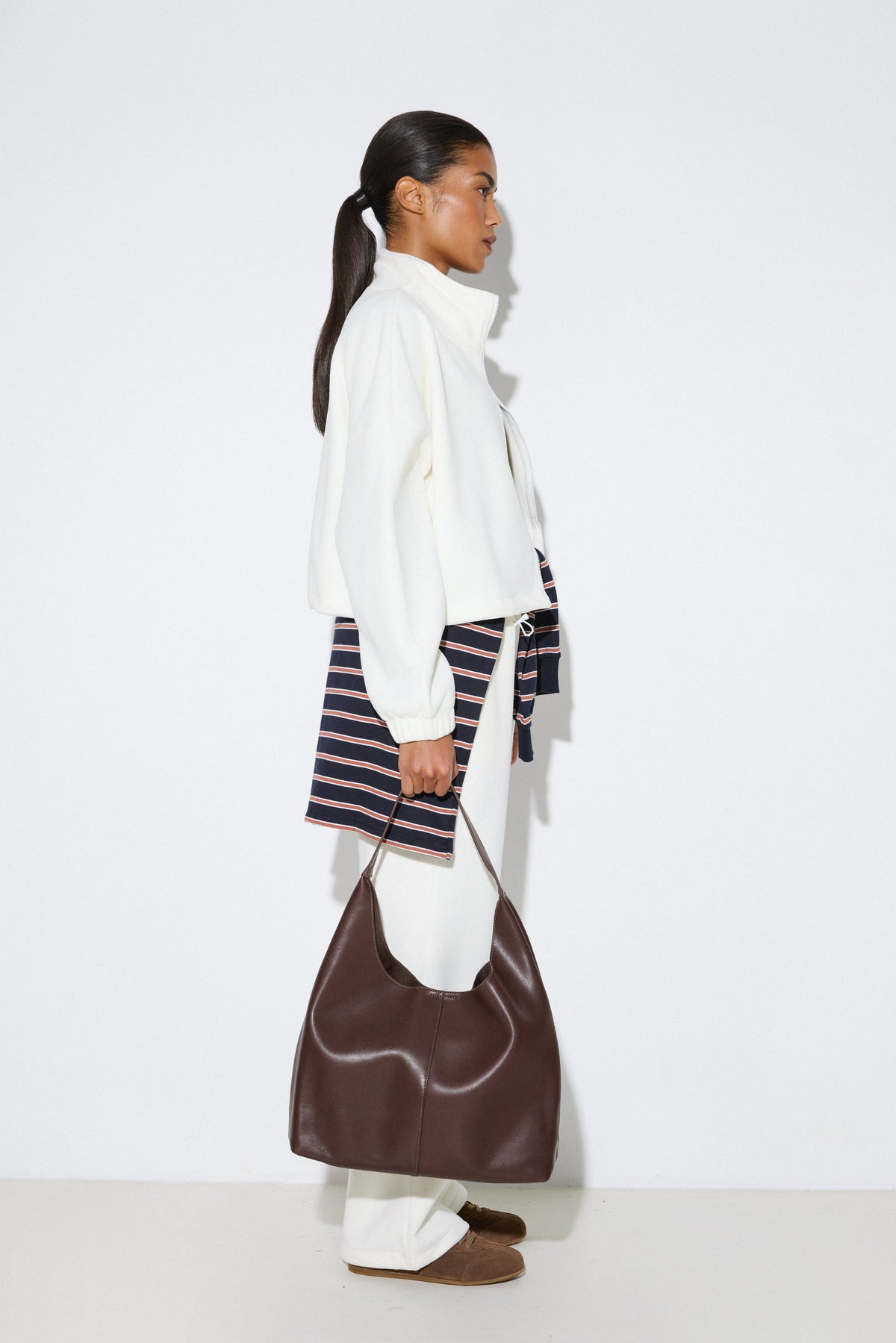 Stilvolle Profilaufnahme eines Models in heller Fleece-Jacke und weißen Hosen, das den dunkelbraunen Damen-Shopper aus echtem Leder präsentiert.