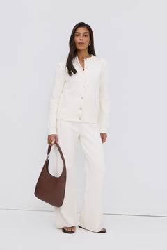 Model steht in einem eleganten weißen Look und präsentiert die dunkelbraune Leder-Shopper-Tasche