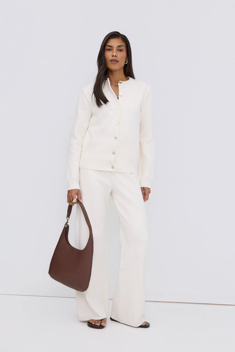 Model steht in einem eleganten weißen Look und präsentiert die dunkelbraune Leder-Shopper-Tasche