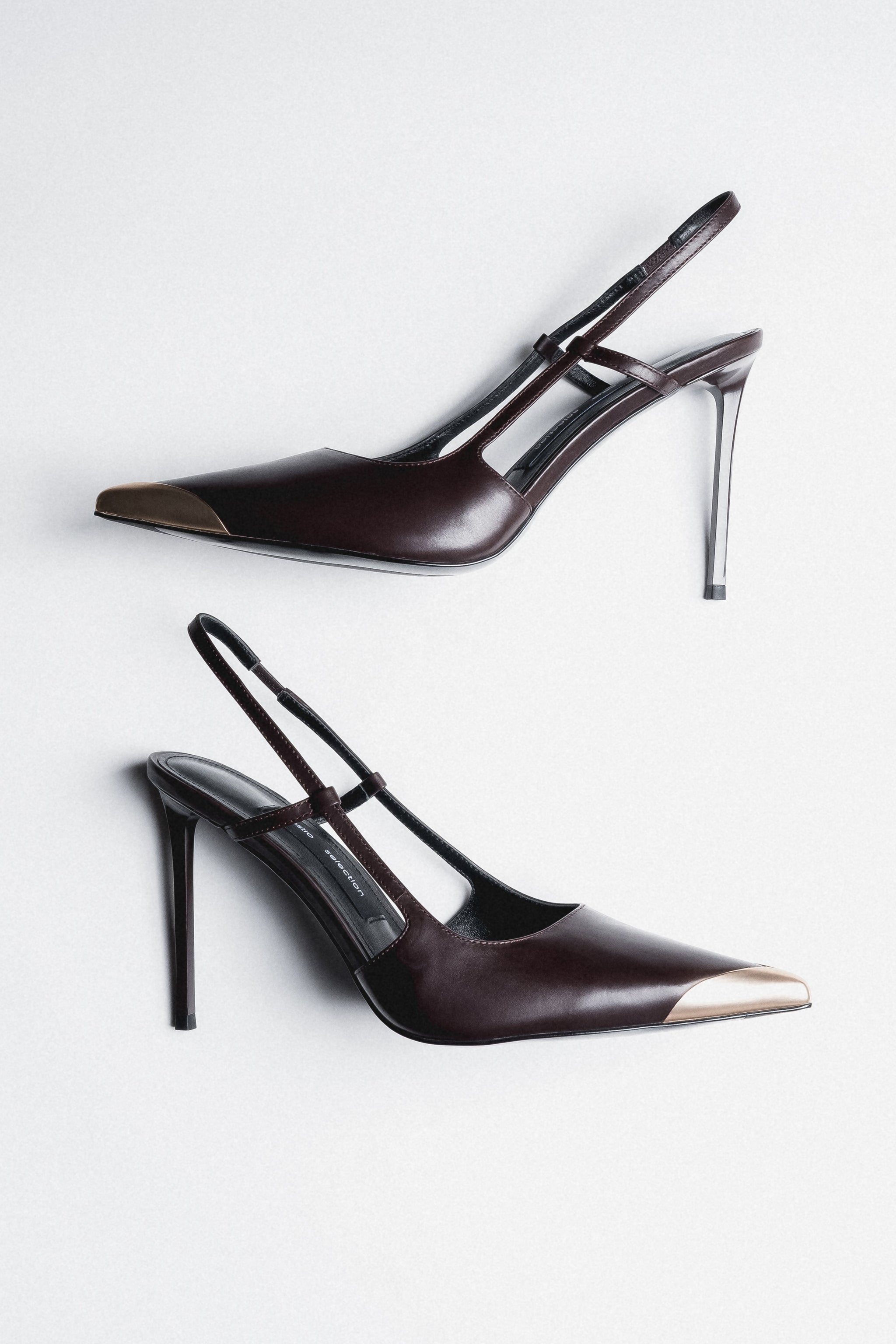 Dunkelbraune Damen-Slingpumps aus Leder als Paar in schräger Seitenansicht mit goldfarbener Spitze
