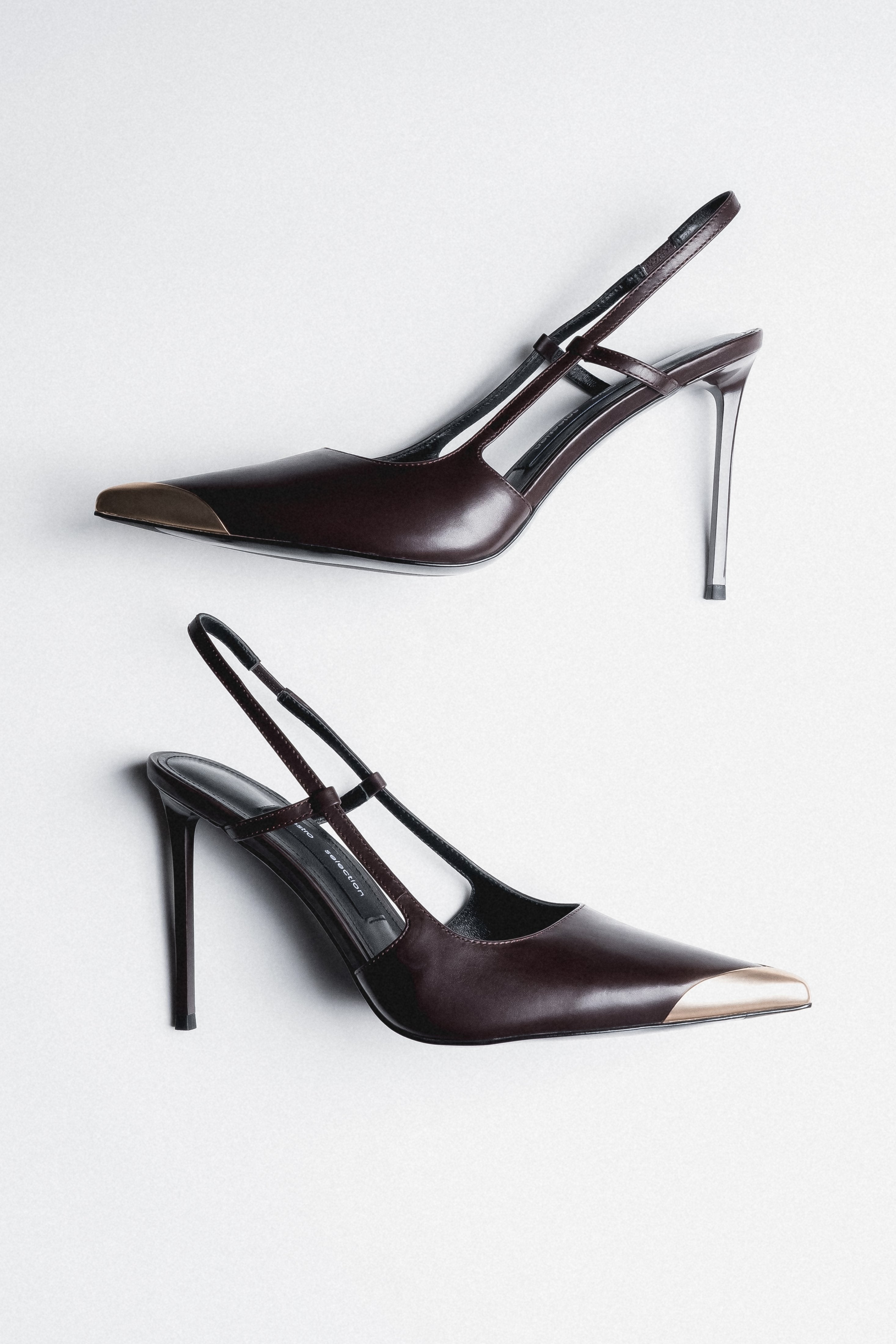 Dunkelbraune Damen-Slingpumps aus Leder als Paar in schräger Seitenansicht mit goldfarbener Spitze