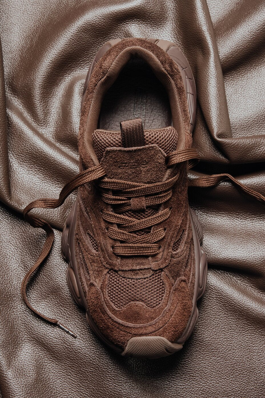 Draufsicht auf braune Chunky-Sneaker aus Veloursleder mit Mesh-Einsätzen und strukturierter Sohle auf einem Ledertuch