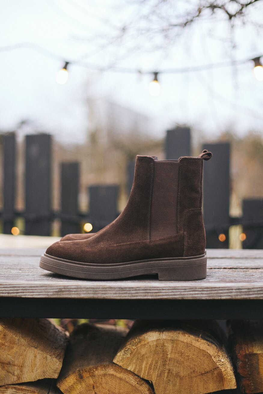 Lifestyle-Aufnahme der dunkelbraunen Chelsea-Boots, ansprechend drapiert auf einer Holzoberfläche im Freien 