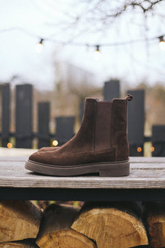Lifestyle-Aufnahme der dunkelbraunen Chelsea-Boots, ansprechend drapiert auf einer Holzoberfläche im Freien 