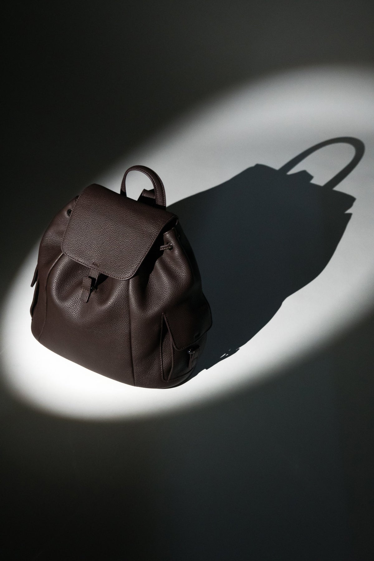 Künstlerische Profilansicht des dunkelbraunen Damen-Beutelrucksacks aus genarbtem Leder im Spotlight