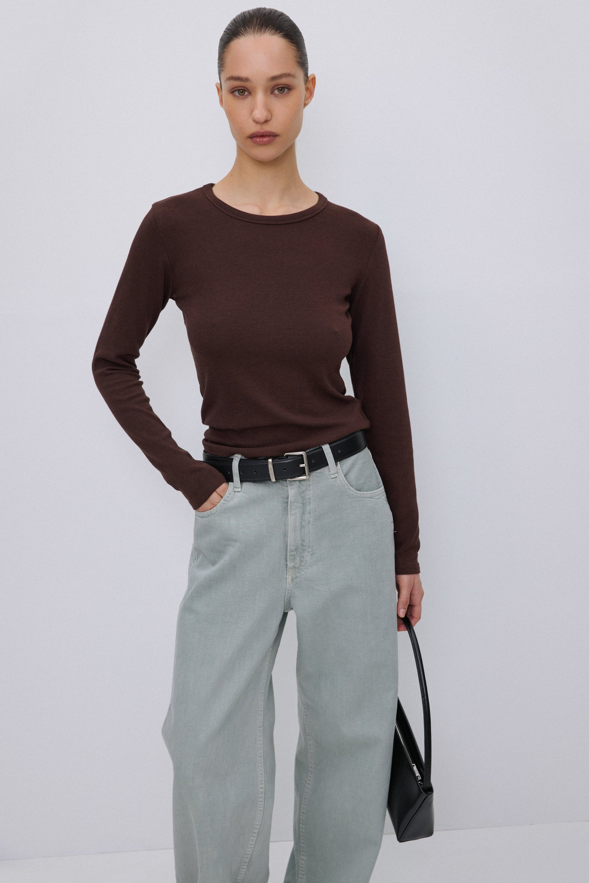 Das Model trägt das dunkelbraune Langarmshirt lässig kombiniert mit einer hellen Hose.