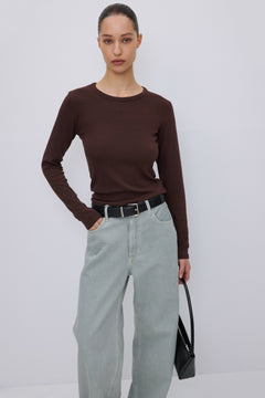 Das Model trägt das dunkelbraune Langarmshirt lässig kombiniert mit einer hellen Hose.