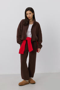 Frontalansicht eines Models in einem dunkelbraunen Damen-Fleece-Set mit einem lässig um die Hüfte gebundenen roten Pullover