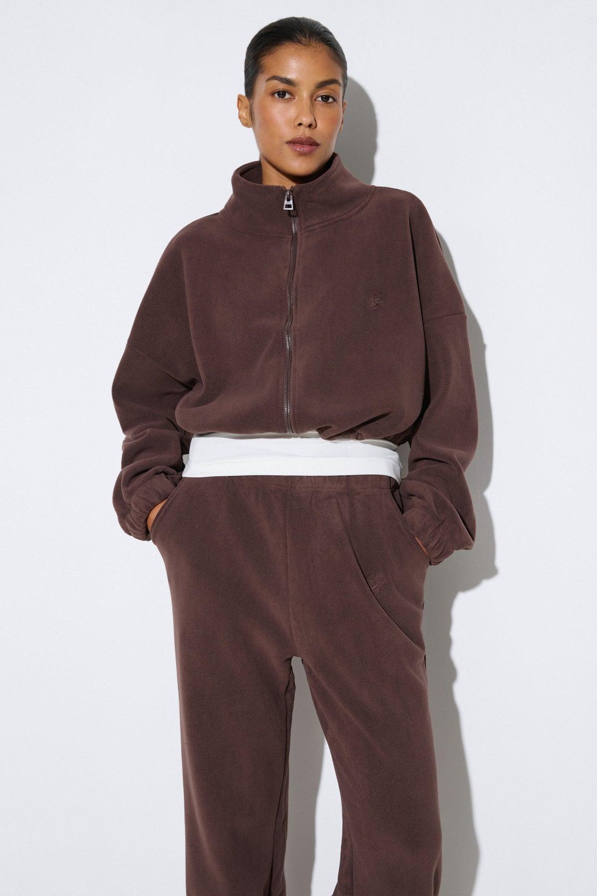 Lifestyle-Aufnahme des Models im dunkelbraunen Fleece-Set mit den Händen in den seitlichen Hosentaschen